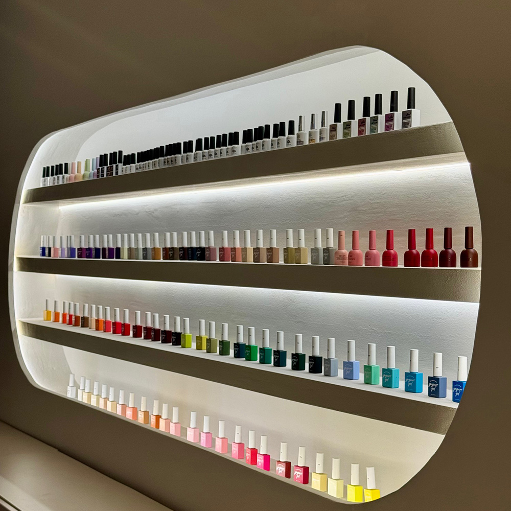 Eine beleuchtete Regalwand mit zahlreichen bunten Nagellackflaschen.