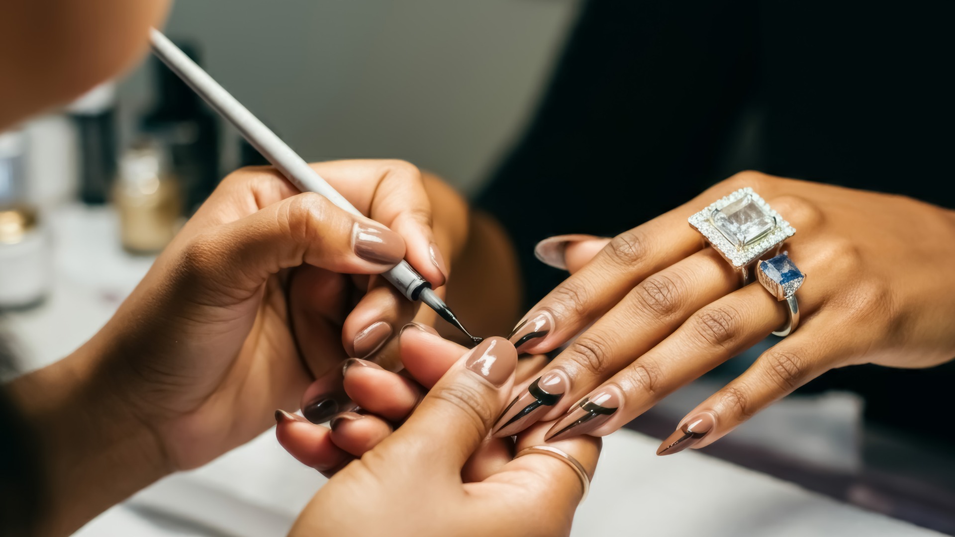 Eine Nagelkünstlerin arbeitet an einer monochromen dunkelbraunen Maniküre mit einem dünnen Liner-Pinsel. Afroamerikanische Frau, die sich in einem Schönheitssalon die Nägel machen lässt, Nahaufnahme.